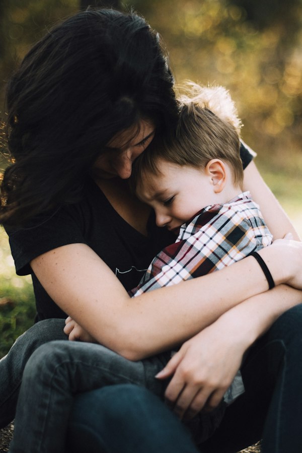 Mother calmly holding and comforting her upset young son outdoors