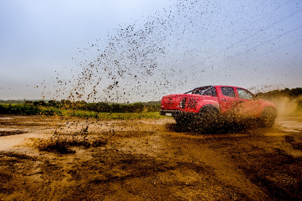 red 4-door truck on mud near trees under cloudy sky