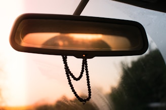 A hanging diffuser swaying gently from a rearview mirror, surrounded by soft sunlight.