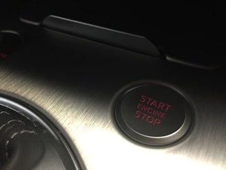A metallic surface with brushed texture featuring a circular button labeled with 'Start Engine Stop' in red text. The area is dimly lit, highlighting the sleek and modern design.