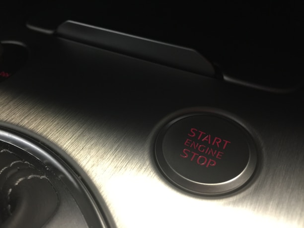 A metallic surface with brushed texture featuring a circular button labeled with 'Start Engine Stop' in red text. The area is dimly lit, highlighting the sleek and modern design.