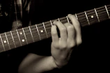 Close-up of Tony’s weathered hands strumming a vintage acoustic guitar, textured leather strap visible.