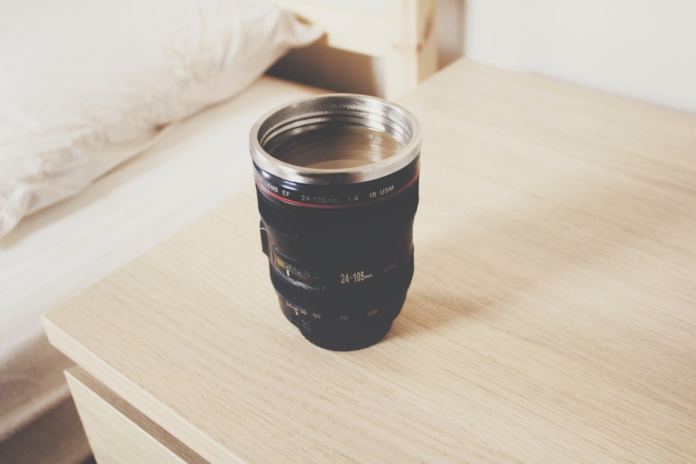 taza de viaje con lente de cámara DSLR negra en mesita de noche