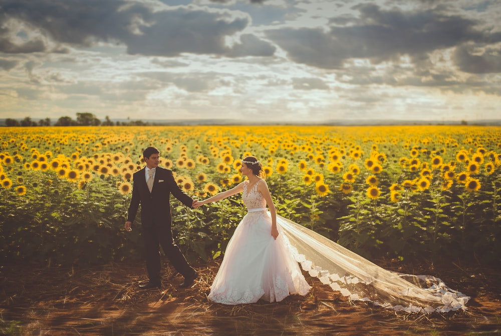 bride and groom walking in front of sunflower field