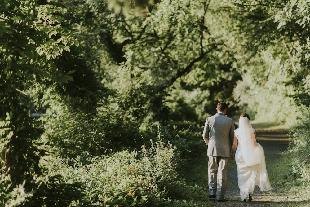 groom and bride walking on forest pathway photograph