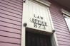 A close-up view of an exterior building wall with horizontal paneling painted in a soft pink color. The central focus is a large rectangular plaque stating 'LAW OFFICE 823' in bold letters. The paneling and design suggest a historical or vintage style.