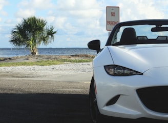A bright white convertible with the top down on a coastal road.