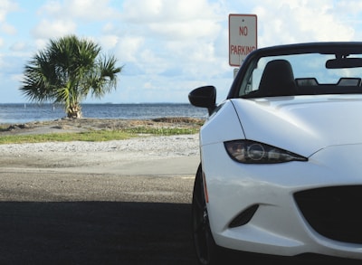 A sleek white convertible parked on a sunlit beach road with turquoise ocean in the background.