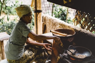 A rustic wooden coffee roasting setup with glowing embers and hands carefully stirring coffee beans over an open flame.
