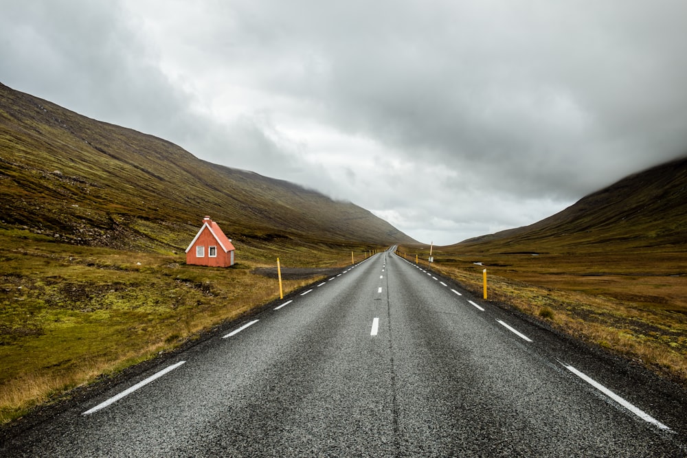 empty gray concrete road top near pink wooden house during cloudy day