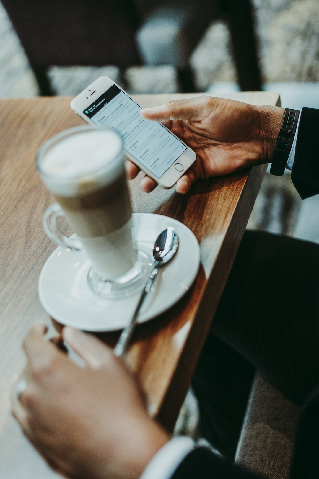 A man in a suit using an iPhone while sitting over a tall coffee
