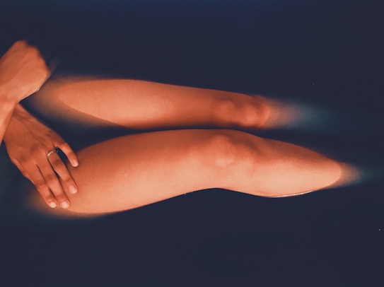 A pair of legs submerged in dark water, with soft lighting creating a calming and serene atmosphere. The person's hand is gently resting on their leg.