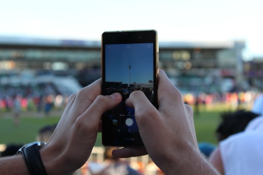 A dynamic photo of a football content creator filming a match highlight on a smartphone in a stadium.