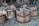 Several wooden buckets with rope handles are positioned on a surface covered with straw. The buckets have a rustic and weathered appearance, showing signs of use and age. The wooden planks of the buckets are bound together with metal hoops.