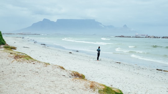 person standing on shore near mountain covering of fogs at daytime in Table View South Africa