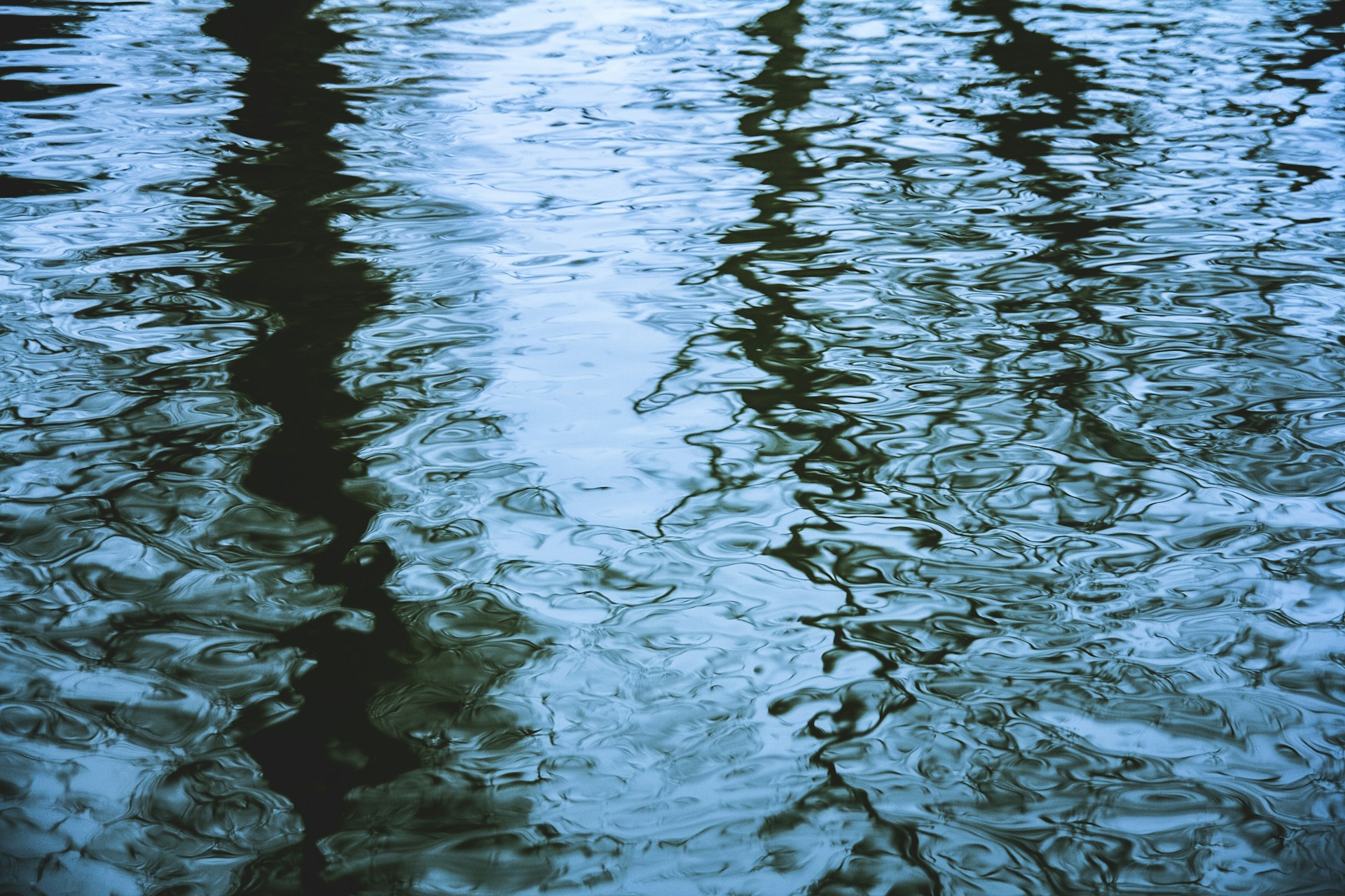 Rippling water reflecting a dramatic sky in shades of deep blue and brown, capturing a moment of quiet reflection.