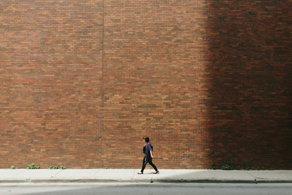 woman in black shirt walking on sidewalk near brown concrete wall partition