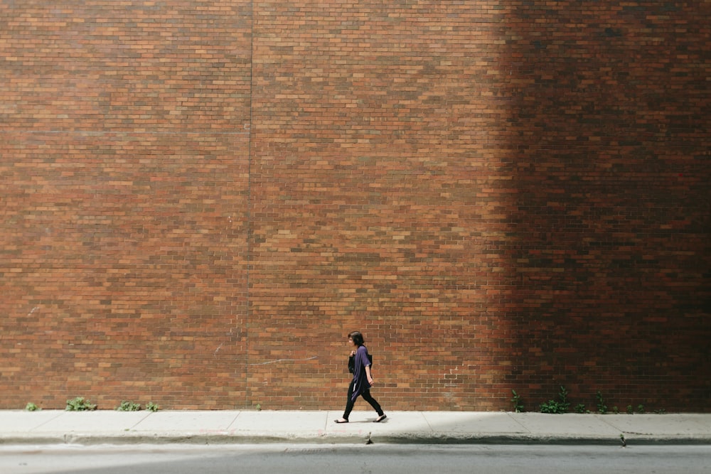 Frau im schwarzen Hemd geht auf dem Bürgersteig in der Nähe der braunen Betonwandwand
