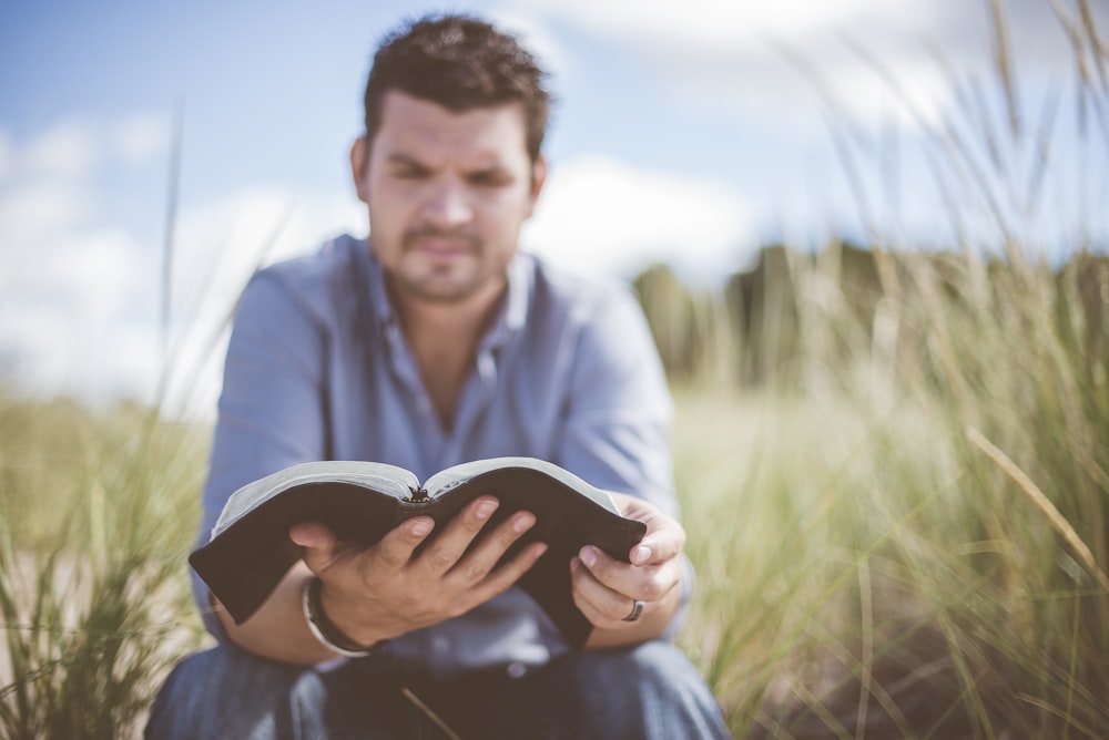 man reading book in grass field