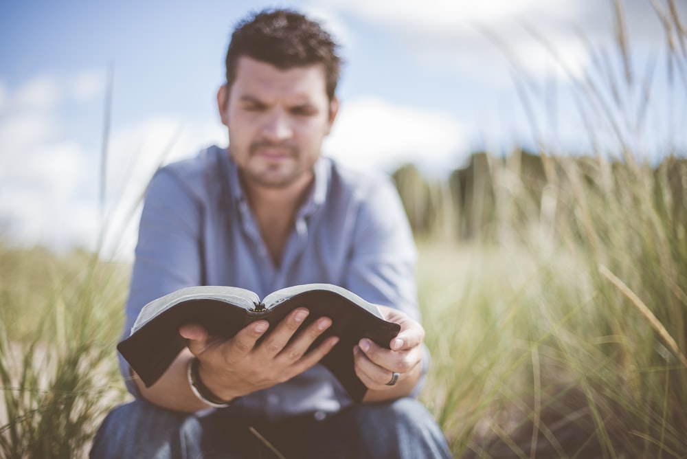 hombre leyendo un libro en un campo de hierba