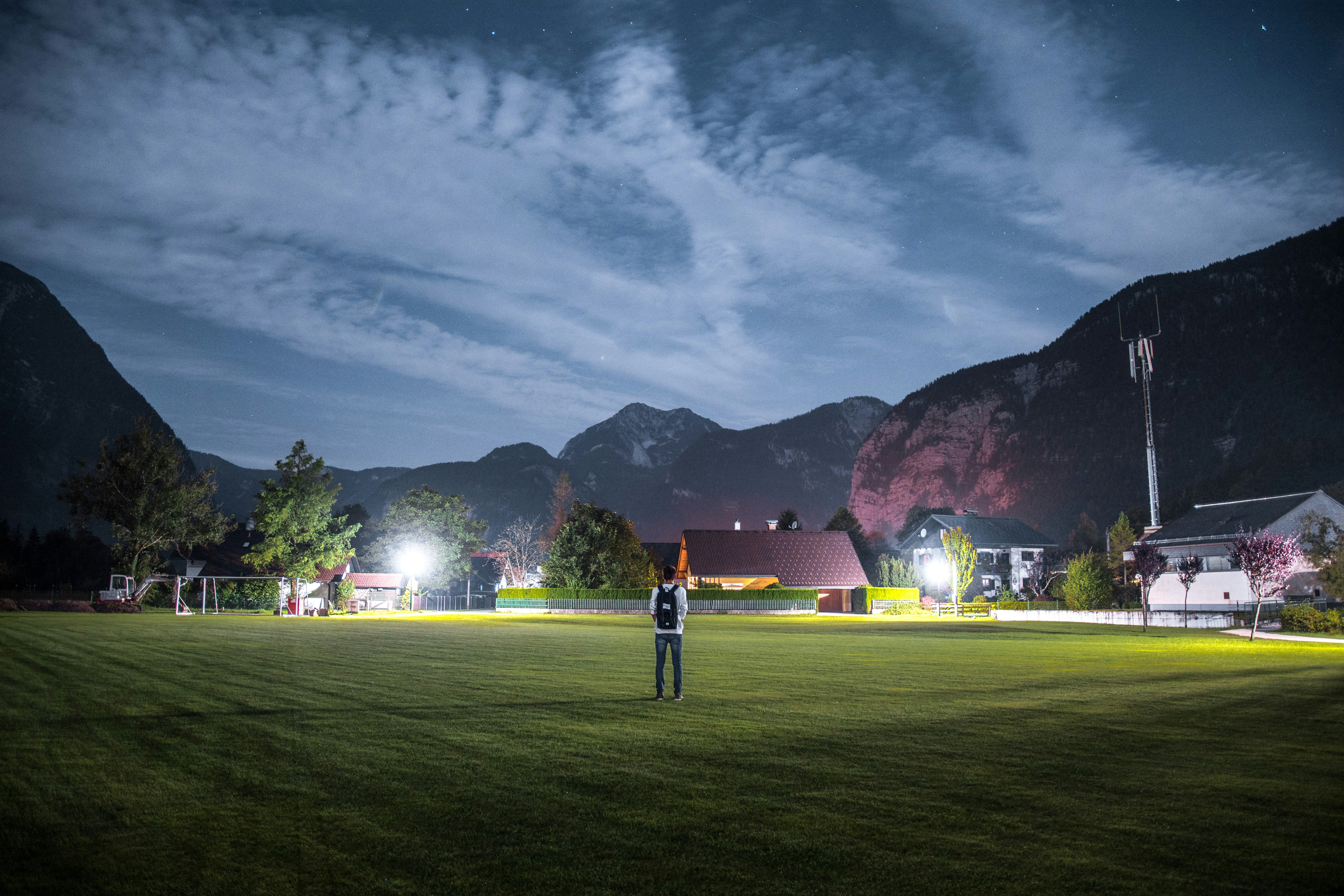 man in white shirt with black backpack standing on green grass field