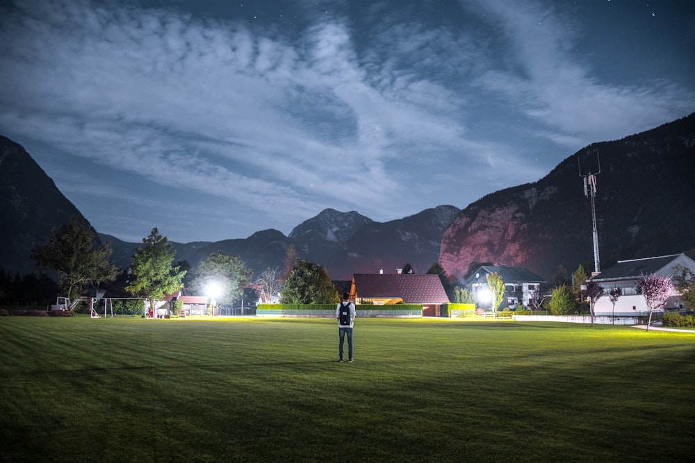 man in white shirt with black backpack standing on green grass field