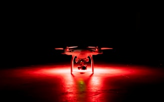 A drone is positioned on the floor, illuminated by a striking red light in an otherwise dark environment.