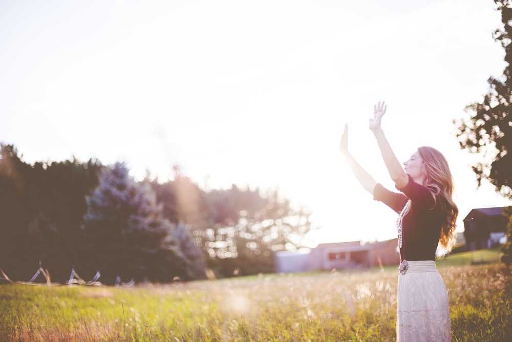 Mujer con las manos levantadas frente a verdes prados