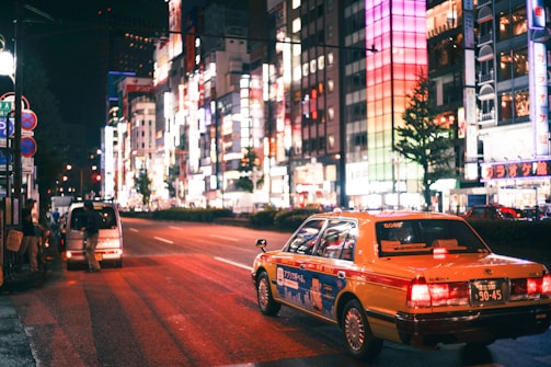A nighttime city street with a taxi car illuminated under streetlights.