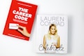 Two books are placed on a white surface. The book on the left is titled 'The Career Code' with a red cover, featuring a hand holding a business card, authored by Hillary Kerr and Katherine Power. The book on the right is titled 'Celebrate' with a white cover, displaying a photograph of a woman holding a cake.