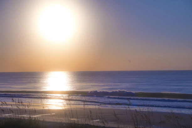 A warm golden sun rising over a calm pacific blue ocean wave, symbolizing connection.