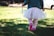 A toddler in a soft pastel outfit running barefoot on fresh grass under sunlight.