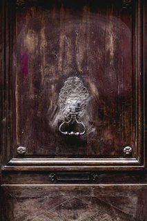A sturdy, classic door with rich mahogany finish and a vintage knocker, set against a brick facade.