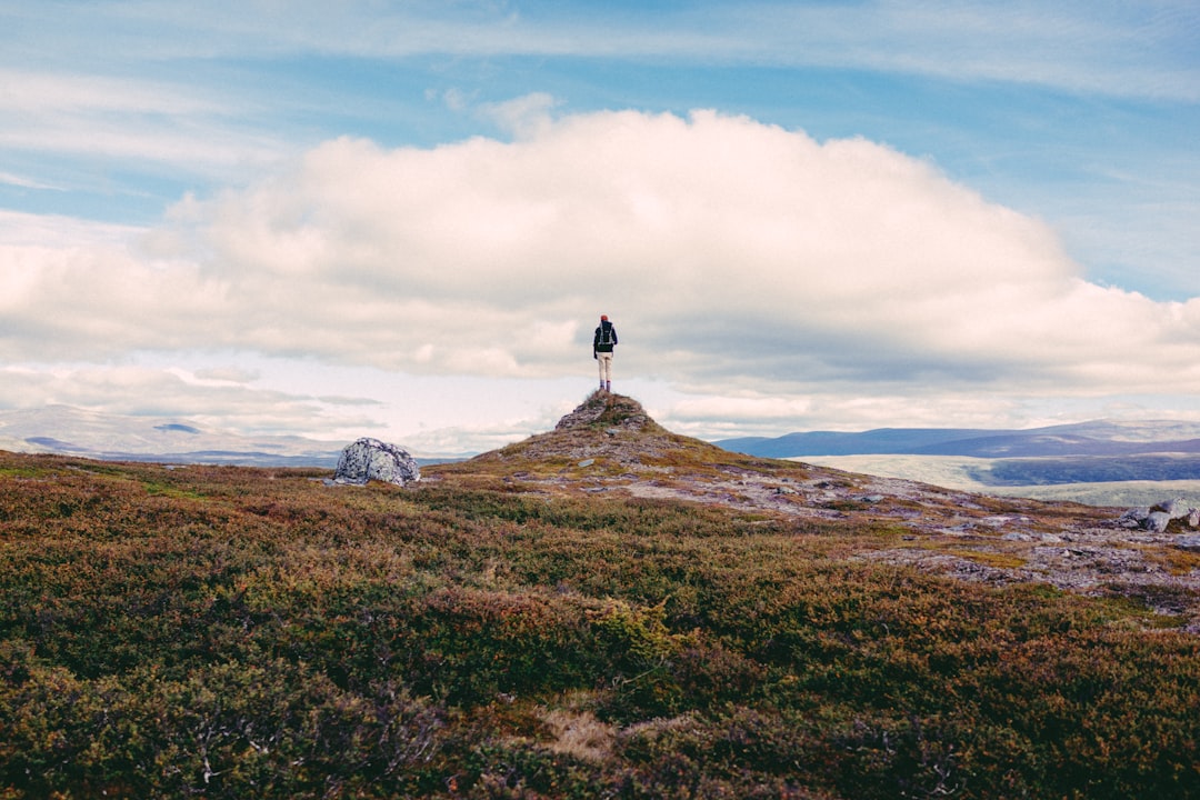 man standing on cliff under white clouds