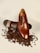 A polished brown leather dress shoe lies atop scattered coffee beans, with its sole partially visible displaying intricate detailing.