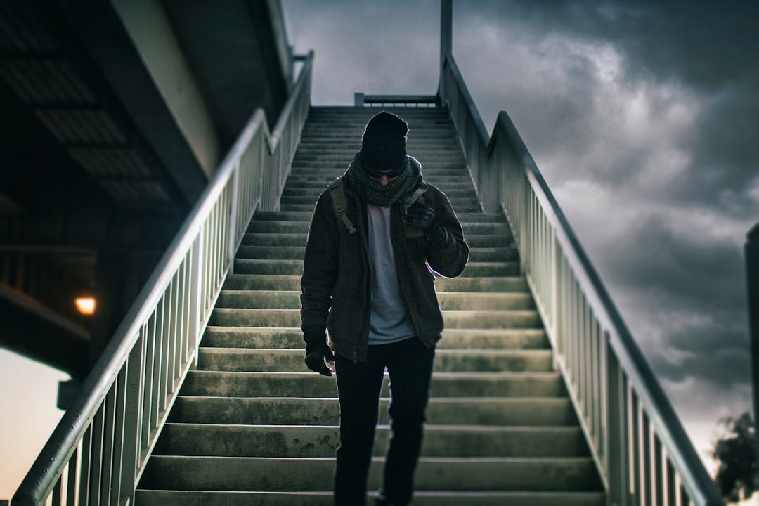 man wearing brown jacket walking on the stair under black sky