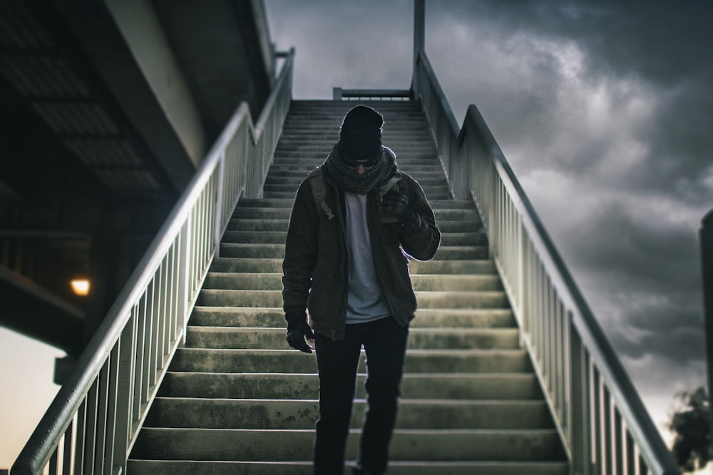 hombre con chaqueta marrón caminando en la escalera bajo el cielo negro