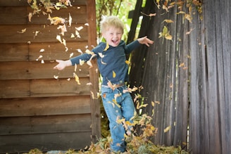 photo of boy near fence with falling leaves