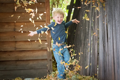 Children laughing as they jump into a pile of crunchy leaves under a clear blue autumn sky.