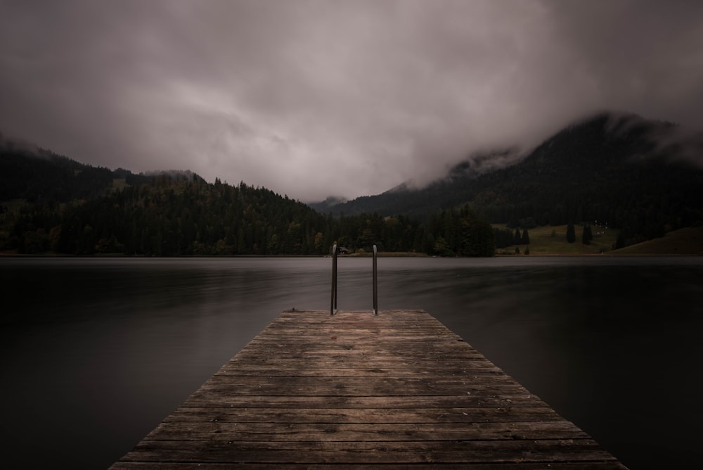 brown wooden dock near lake under cloudy sky