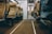 An interior view of a train cabin featuring rows of empty brown leather seats on either side of a central aisle. The seating appears to be in a business class section, as indicated by a sign. The flooring is carpeted in brown with white lines marking the center of the aisle. There is a sliding glass door at the end of the aisle leading to another section of the train.