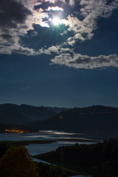 A serene night sky over a peaceful Moonhaven landscape with soft glowing lights.