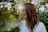 Photo of a relaxed woman outdoors, surrounded by soft greenery, radiating warmth and ease.