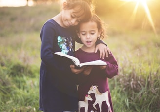 girl's left hand wrap around toddler while reading book during golden hour