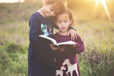 girl's left hand wrap around toddler while reading book during golden hour