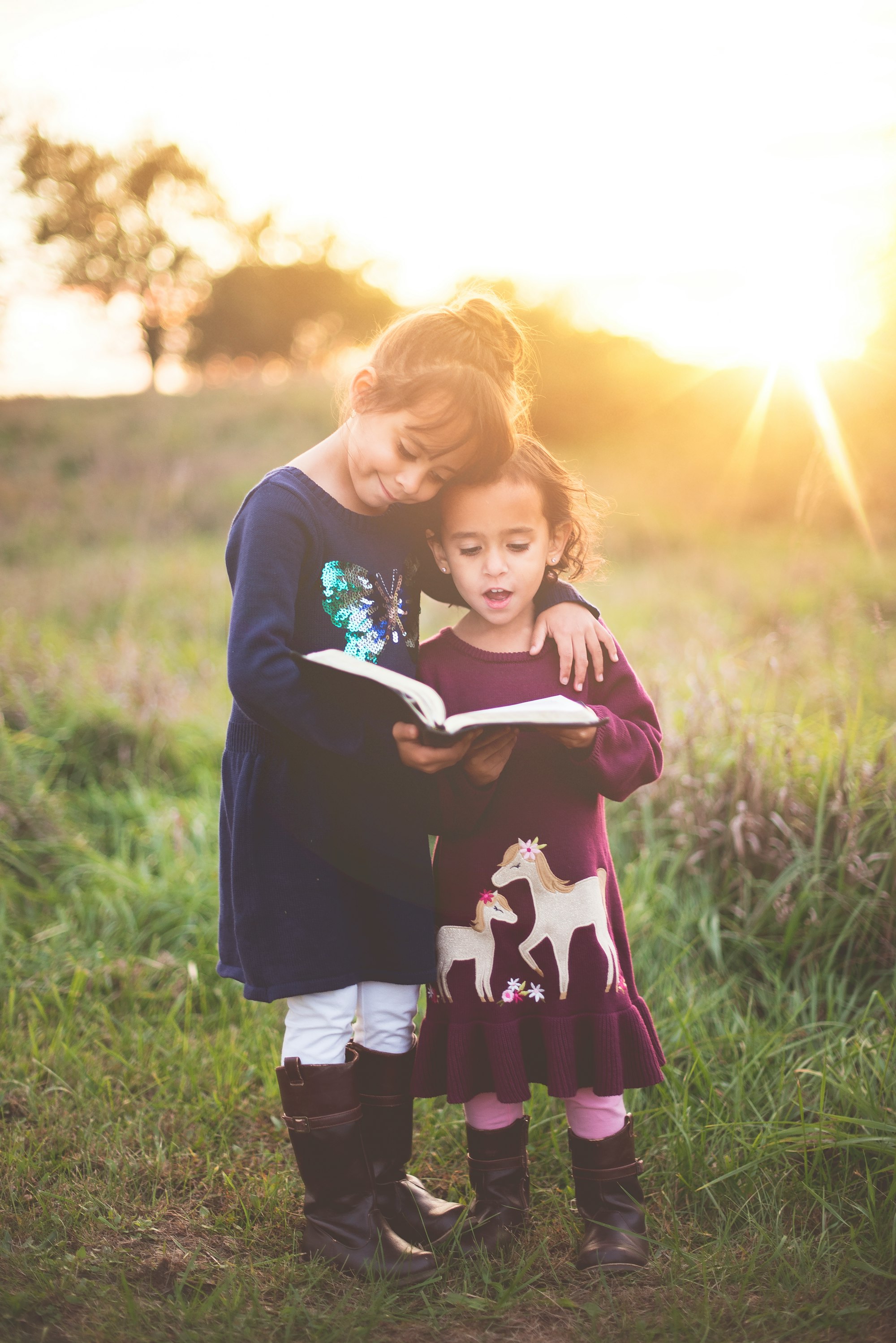 girl's left hand wrap around toddler while reading book during golden hour