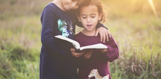 girl's left hand wrap around toddler while reading book during golden hour