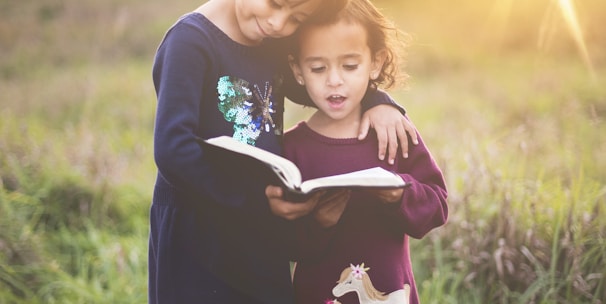 girl's left hand wrap around toddler while reading book during golden hour