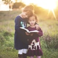 girl's left hand wrap around toddler while reading book during golden hour