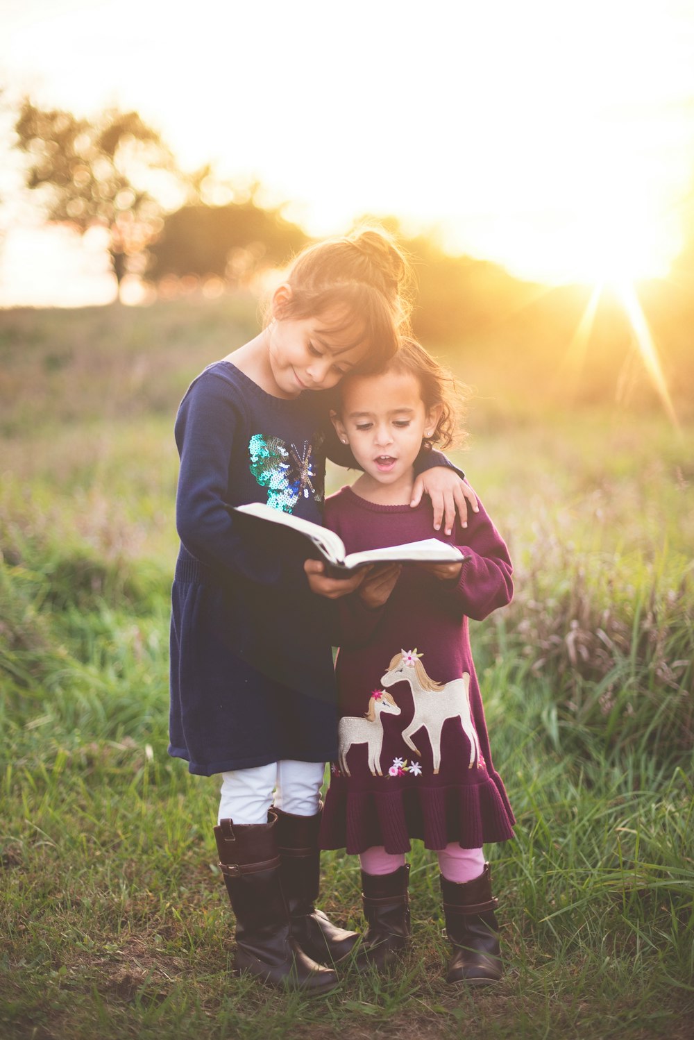 Two young girls stand reading from a book outdoors in the sun